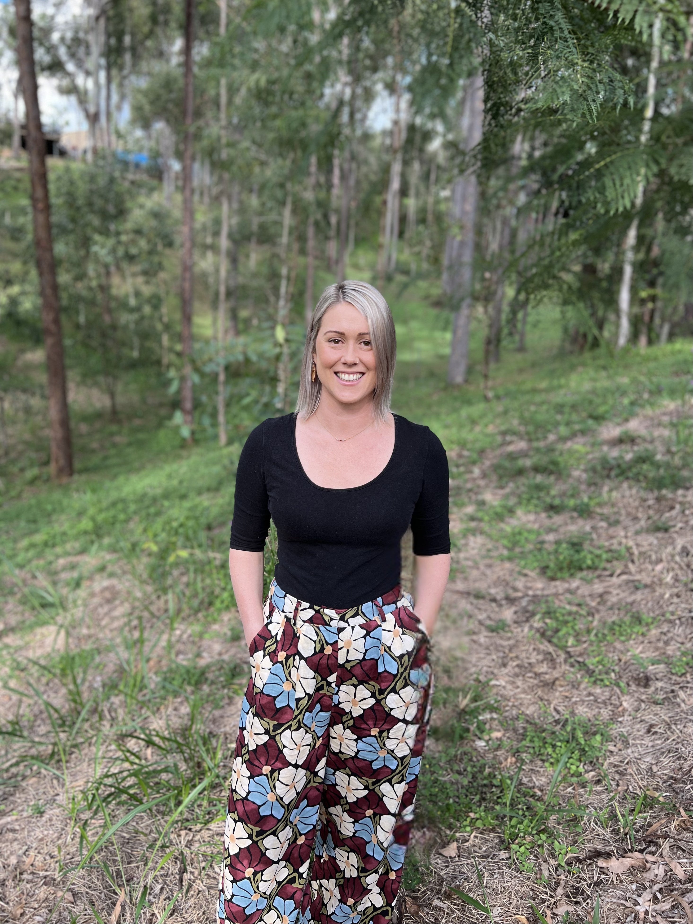 Woman standing in a forest wearing a black top and patterned pants