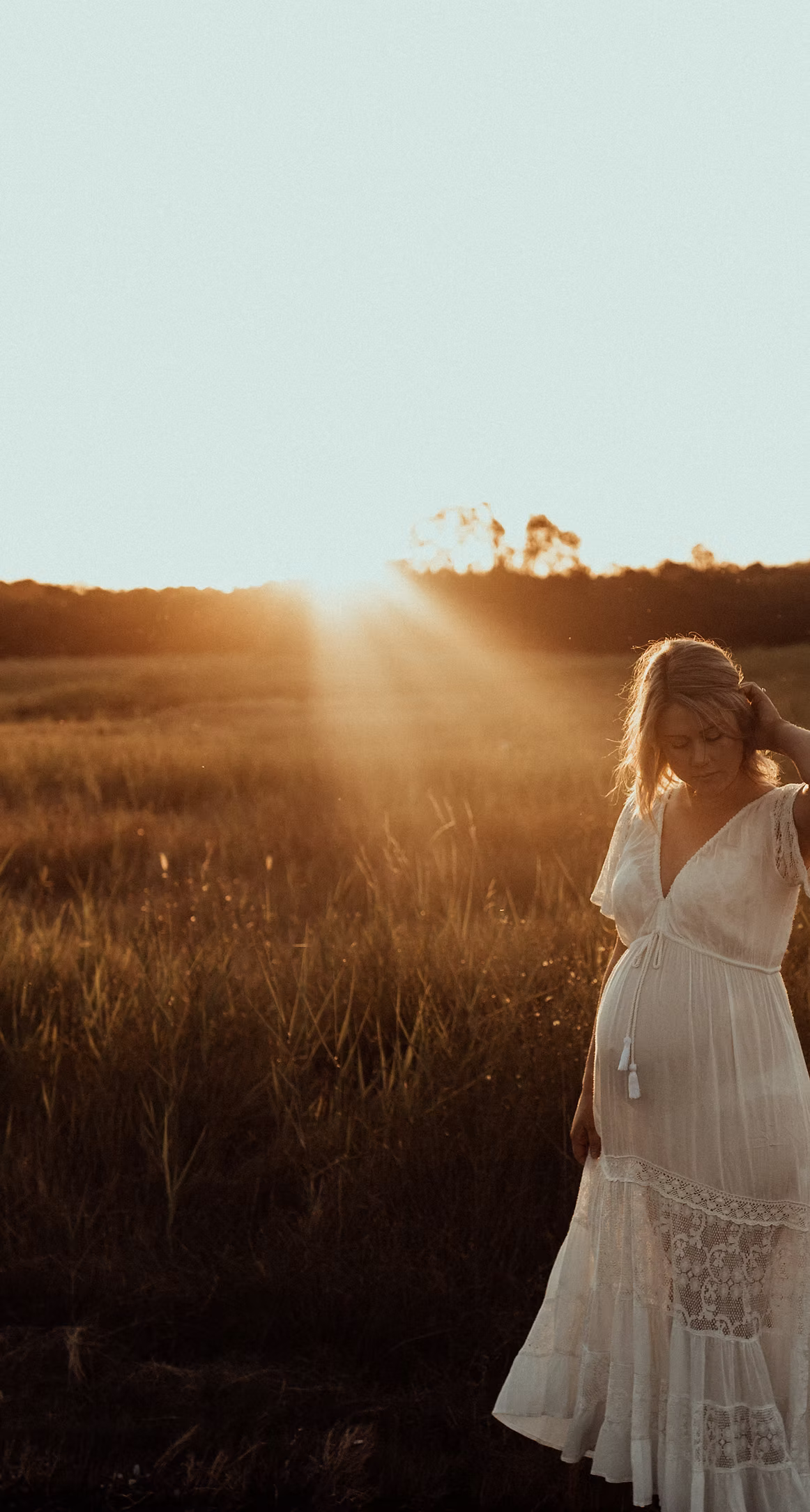 Woman in a white dress standing in a field with sunlight filtering through on the sunshine coast